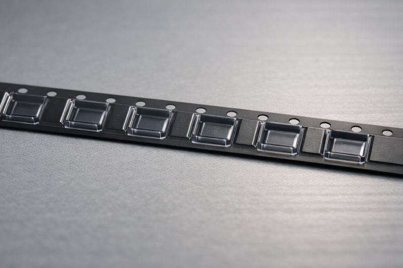 Embossed carrier tape showing pocket center spacing and indexing hole alignment for pitch calculation reference.